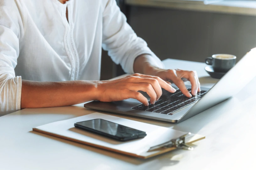 Homem digitando no notebook com o celular ao lado, mostrando como usar o Instagram para vender gás de cozinha
