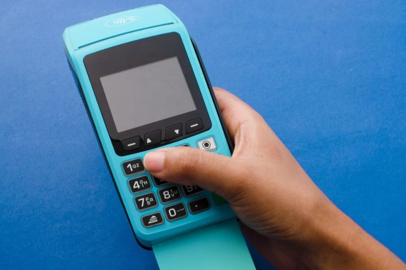 Imagem de uma mão segurando uma máquina de cartão na cor azul, destacando recursos de pagamento sem contato.