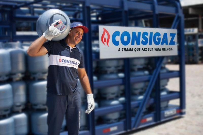 Funcionário da Consigaz carregando um botijão de gás na área de armazenamento.