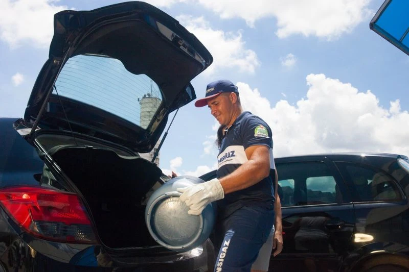 Homem realizando entrega de gás, colocando botijão em um carro.