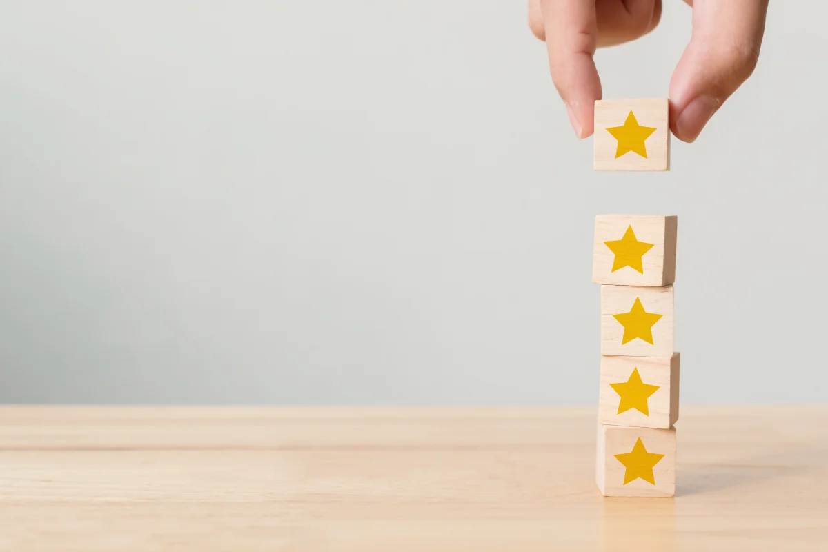 Mão empilhando blocos de madeira com estrelas amarelas representando avaliação de cinco estrelas para texto sobre estratégias de pós-venda.