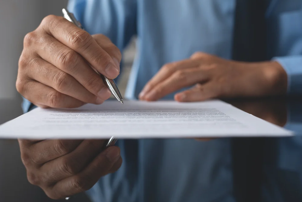 Pessoa assinando certificado de revenda GLP com caneta prateada em mesa refletiva