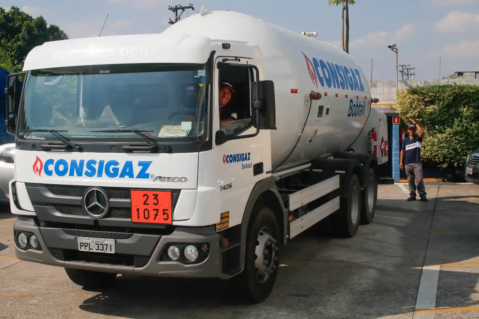 Caminhão-tanque branco da empresa Consigaz estacionado em área industrial, com adesivo de “mercado de energia” e logística de transporte de gás ao fundo.