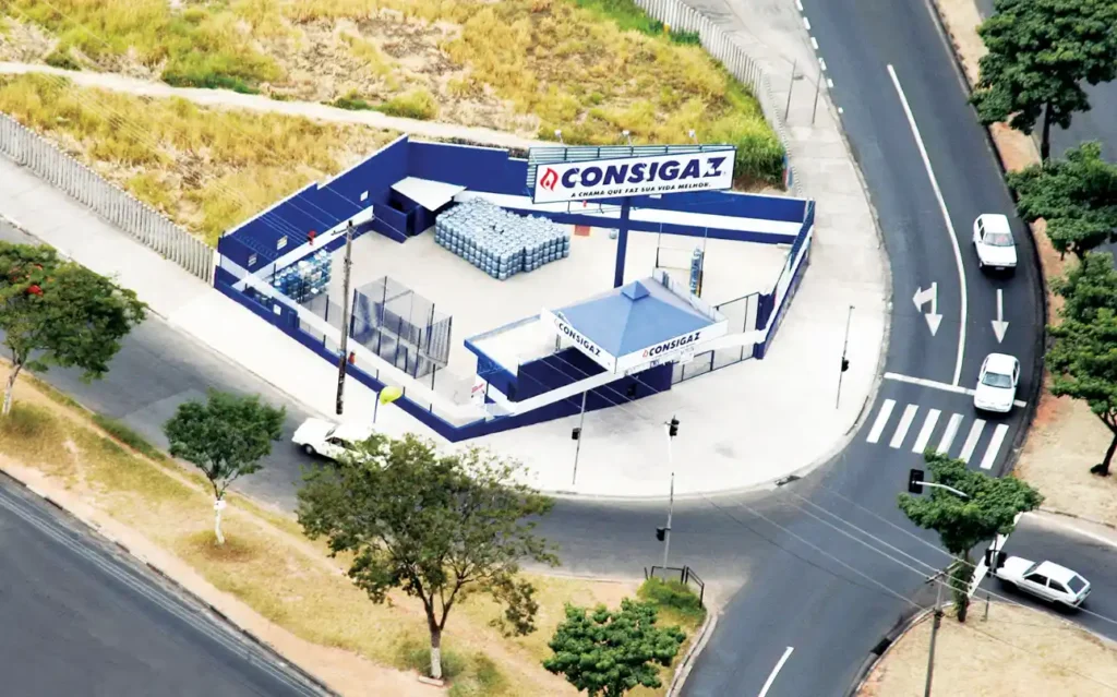 Vista aérea de um centro de distribuição com placas da marca Consigaz, incluindo área interna com armazenamento de botijões e acesso por vias urbanas, destacando marcas de gás de cozinha.