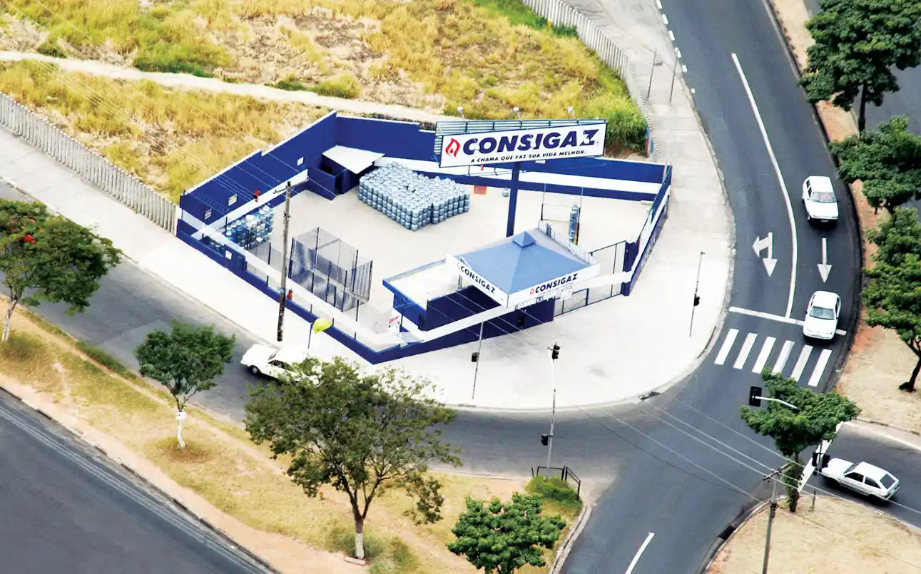 Vista aérea de um centro de distribuição com placas da marca Consigaz, incluindo área interna com armazenamento de botijões e acesso por vias urbanas, destacando marcas de gás de cozinha.
