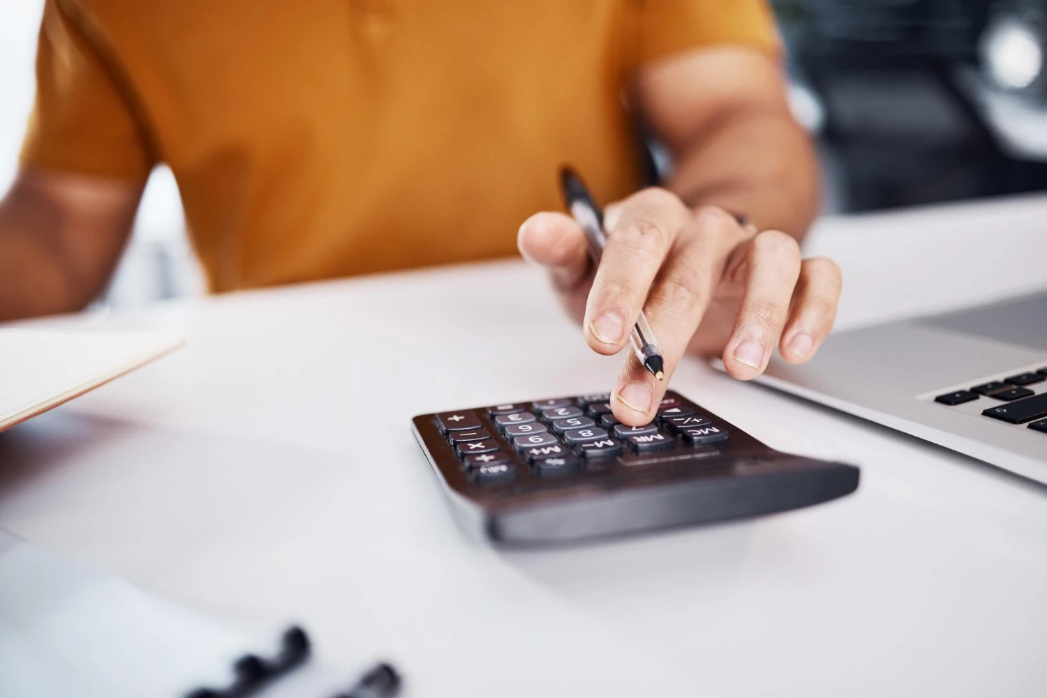 Pessoa em mesa de trabalho utilizando calculadora e caneta para registrar dados financeiros, em ambiente de escritório, com foco na contagem de valores e controle de custos, franquia sem royalties